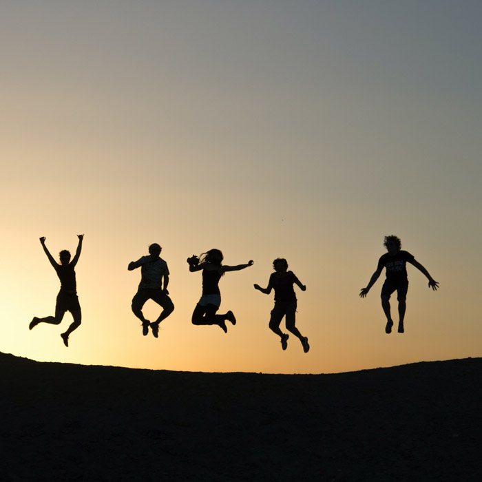 Cinq personnes sautent ensemble, en silhouette, sur un ciel de coucher de soleil
